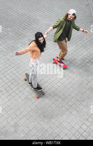 high angle view of happy couple holding hands, smiling and riding on skateboards Stock Photo