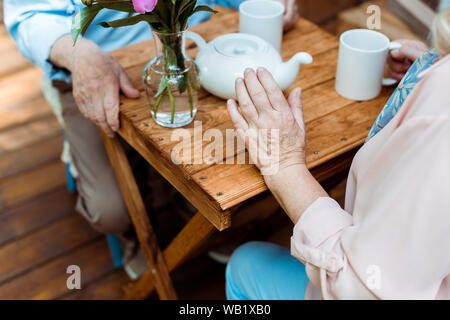 cropped view of retired couple sitting near teapot and cups