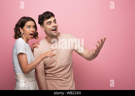 young, excited man and woman smiling and looking away on pink background Stock Photo