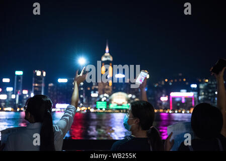 Protesters shine their phone lights while facing the harbour during the demonstration.Protesters held hands to create long human chains in peaceful protest against the extradition bill. Some protesters carried various placards asking and thanking other countries for their support while others also shined their phone lights as a sign of unity and peace. Stock Photo