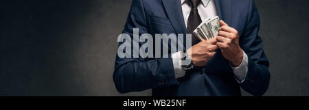 panoramic shot of businessman in suit putting cash in pocket on grey Stock Photo