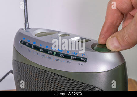 Close shot of a man’s hand turning a rotary control to tune in a station on a traditional old analog radio. Stock Photo