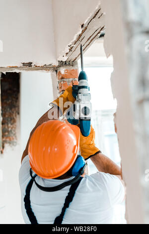 back view of handyman using hammer drill on wall Stock Photo
