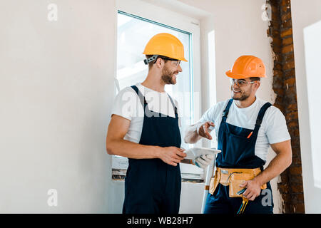 cheerful repairman in goggles looking at coworker while holding digital tablet Stock Photo
