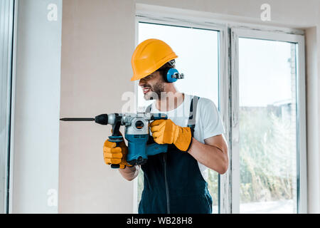 handyman in uniform and yellow gloves using hammer drill Stock Photo