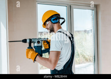 handyman in helmet and yellow gloves using hammer drill Stock Photo