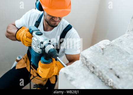 overhead view of handyman in helmet and yellow gloves using hammer drill Stock Photo