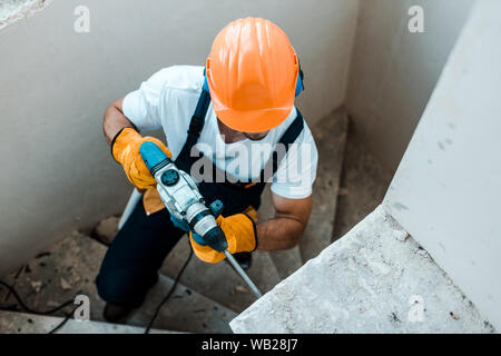 overhead view of workman in uniform and yellow gloves using hammer drill Stock Photo
