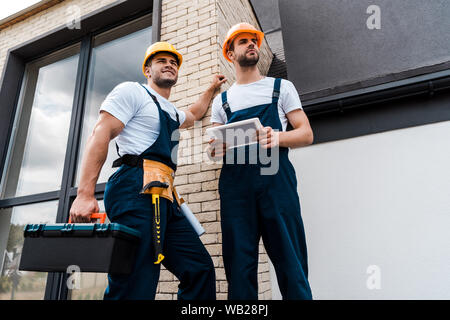 low angle view of handsome handyman holding toolbox near coworker with digital tablet Stock Photo