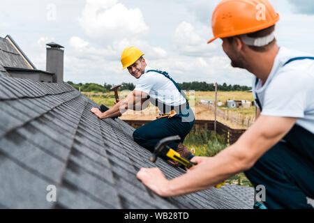 selective focus of happy repairman looking at coworker on roof Stock Photo