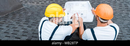 panoramic shot of builders in helmets looking at blueprint Stock Photo
