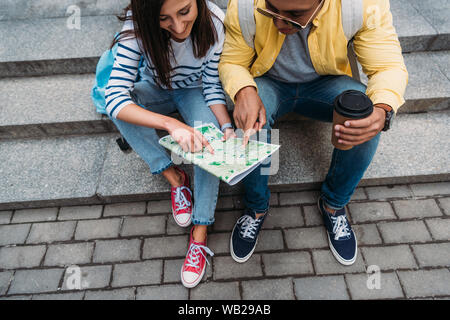 Bi-racial man pointing with finger on map near woman sitting on stairs Stock Photo