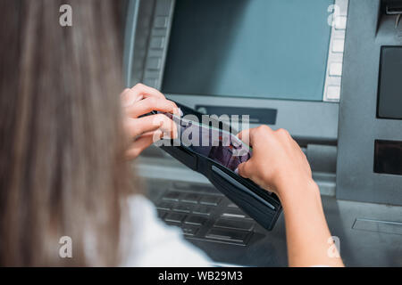 cropped view of woman putting money in wallet near atm machine Stock Photo