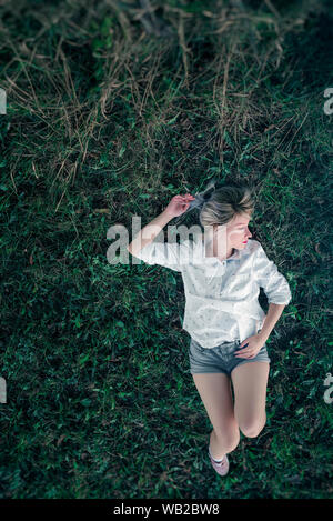 Young woman laying in grass in white shirt and makeup Stock Photo