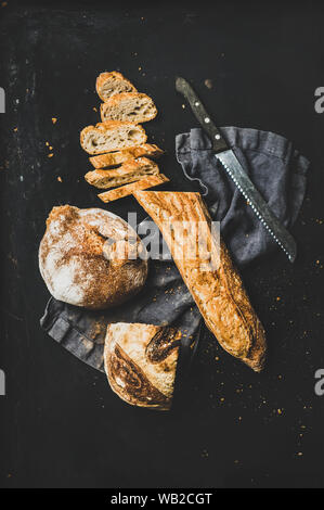 Flat-lay of baguette in slices and loaf over black background Stock Photo