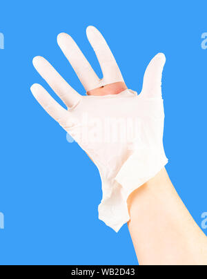 broken white latex surgeon medical glove on caucasian hand isolated on blue monocolor background. Stock Photo