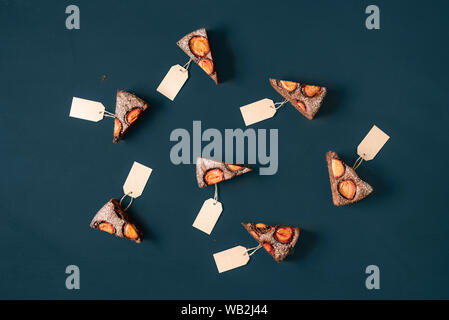 Slices of chocolate cake with plums, each with blank labels on a blue background. Above view of pie slices with unwritten tags. Pattern of cake slices Stock Photo