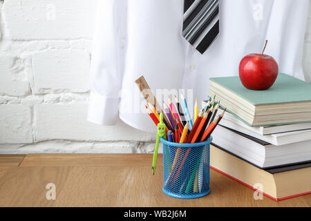 School supplies, a stack of books and apple on the table against the background of a white shirt with a tie on a hanger, soft focus Stock Photo