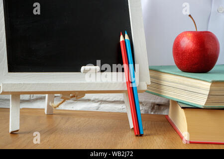 School supplies, miniature chalk board, a stack of books and apple on the table, soft focus Stock Photo