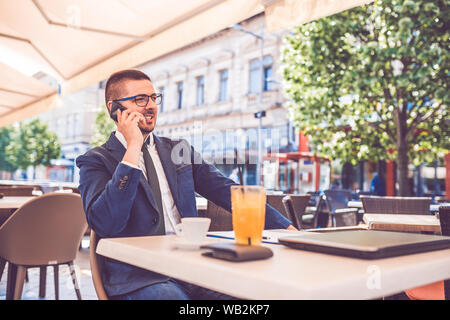 Portrait of excited entrepreneur in glasses working on business project in city cafe, talking on the phone Stock Photo