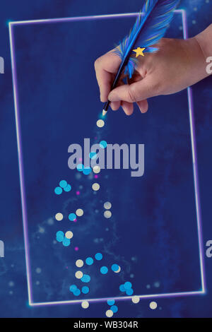 Christmas or New Year creative concept. Female hand drawing trail of paper snowflakes from blue feather quill on dark blue paper background with glowi Stock Photo