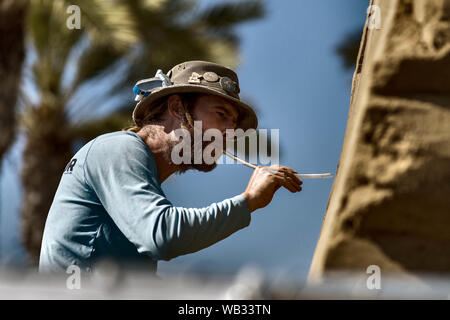 San Diego, California, USA. 23rd Aug, 2019. Canadian sand sculptor ABE WATERMAN works on a sculpture commemorating the 250th anniversary of the founding of San Diego, California. By blowing air through the plastic tube, he can remove small bits of sand without disturbing the sculpture. Credit: David Barak/ZUMA Wire/Alamy Live News Stock Photo