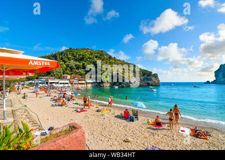 Tourists relax and swim in the clear turquoise waters and on the sandy Palaiokastritsa beach on the Aegean island of Corfu, Greece. Stock Photo