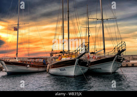 Three beautiful yachts sit at the dock in Kas, Turkey as the sun glows in the background Stock Photo