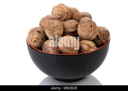 A black bowl filled with whole walnuts in their shells on a white background. Stock Photo
