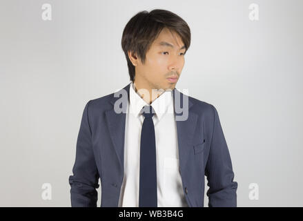 Young Asian Portrait Businessman in Navy Blue Suit Looking Below on Grey Background Stock Photo