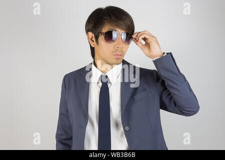 Young Asian Portrait Businessman in Navy Blue Suit Touch Sunglasses and Look Above on Grey Background Stock Photo