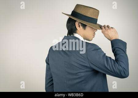 Young Asian Portrait Businessman in Navy Blue Suit Touch Hat at Back View on Grey Background Stock Photo