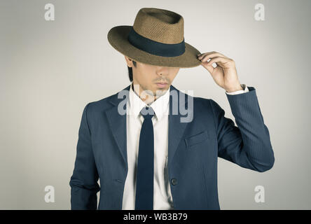Young Asian Portrait Businessman in Navy Blue Suit Touch Hat Brim at Front View on Grey Background Stock Photo