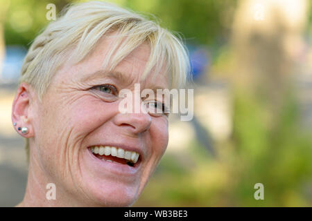 Close up portrait of an attractive older blond laughing woman outdoors in a park Stock Photo