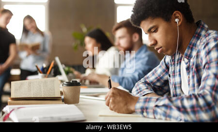 African-american guy preparing for exam, taking notes in library Stock Photo