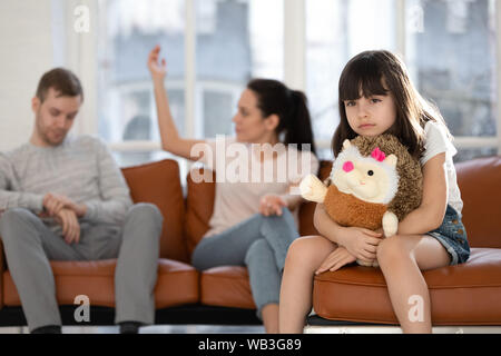 Sad child daughter holding toy feeling hurt about parents arguing Stock Photo