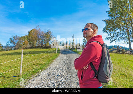 A man with a backpack on a country road among autun colored nature Stock Photo