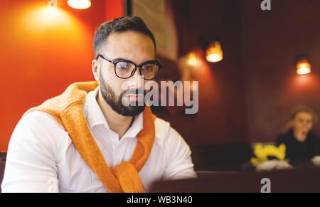 Concentrated young man wearing glasses typing on laptop in cafe Stock Photo
