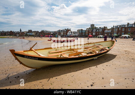 North Berwick, Scotland, UK, 24 August 2019. Colourful rowing skiffs taking part in the regatta from 12 clubs across Scotland compete on a hot sunny bank holiday weekend. The St Ayle's skiff is a traditional 4 oared rowing boat. Pictured: The Dunbar coastal rowing team's boat named Black Agnes pulled onto the beach Stock Photo