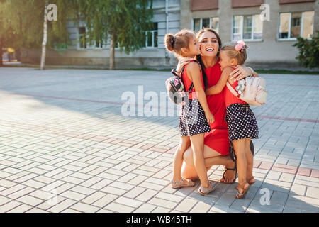 Happy mother meeting her kids daughters after classes outdoors primary school. Family hugging. Back to school concept Stock Photo