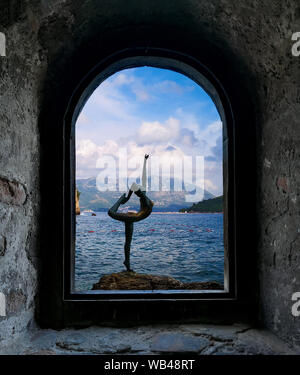 From the rock window: Statue of a ballerina Dancer of Budva against the Old Town of Budva near Mogren beach fortress, Budva, Montenegro. Stock Photo