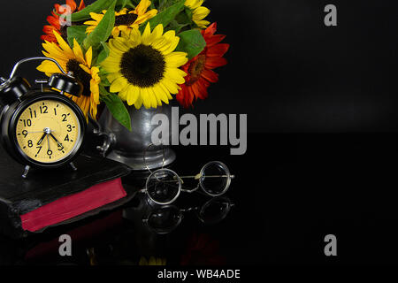 sunflower bouquet in vintage pewter jug with Bible and old eyeglasses on black reflection Stock Photo