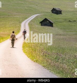 Two hikers on the road through the Tschey meadows, in Pfunds, Tyrol, Austria Stock Photo