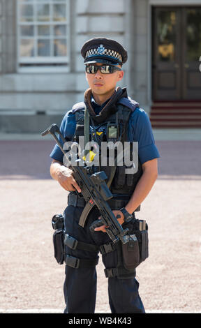 Male armed Metropolitan Police officer carrying a gun outside Buckingham Palace in City of Westminster, Central London, England, UK. Stock Photo