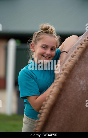 Portrait of a young equestrian girl standing next to her braided horse at a horse show  and smiling at the camera Stock Photo