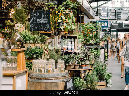 Denmark, Copenhagen - July 20th, 2016: People browsing the halls of Torvehallerne Market, surrounded by green plants. Stock Photo
