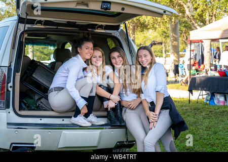 A group of high school equestrian girls are posing for the camera together  from the trunk of a car at a horse show Stock Photo