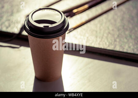 Disposable coffee cup on the rough art studio table next to paint brushes. Arty colorful and creative mood. Stock Photo