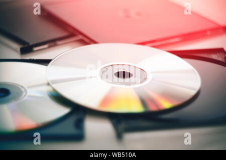Two disks lie in black plastic packages for disks and gleam in different colors, illuminated by a bright red light. Stock Photo