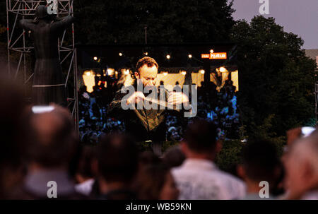 Berlin, Germany. 24th Aug, 2019. On a screen on the Straße des 17. Juni, people follow the open-air concert of the Berliner Philharmoniker under the direction of the new chief conductor Kirill Petrenko (M). Credit: Paul Zinken/dpa/Alamy Live News Stock Photo